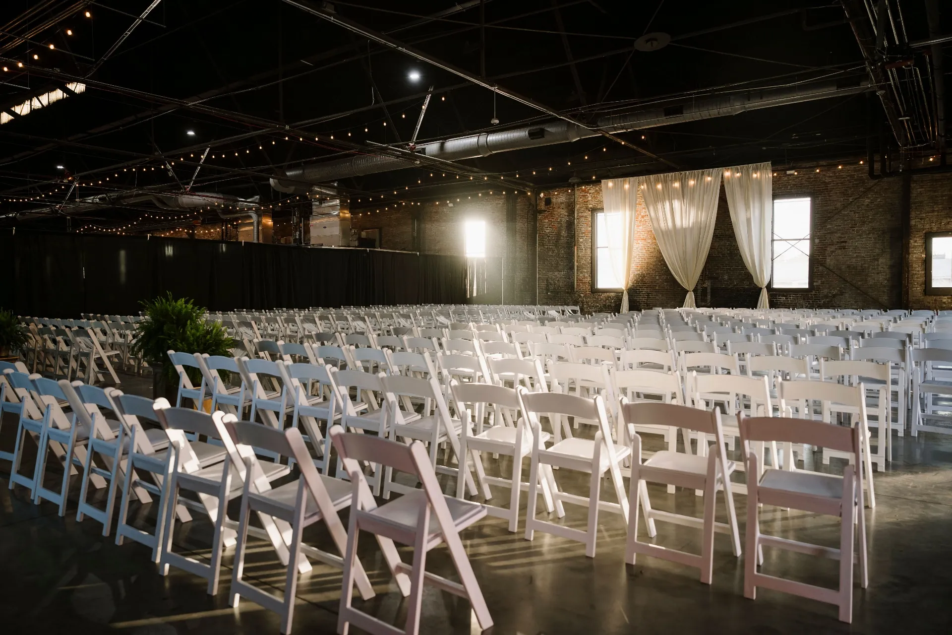 Rows of white folding chairs set for ceremony with draped backdrop