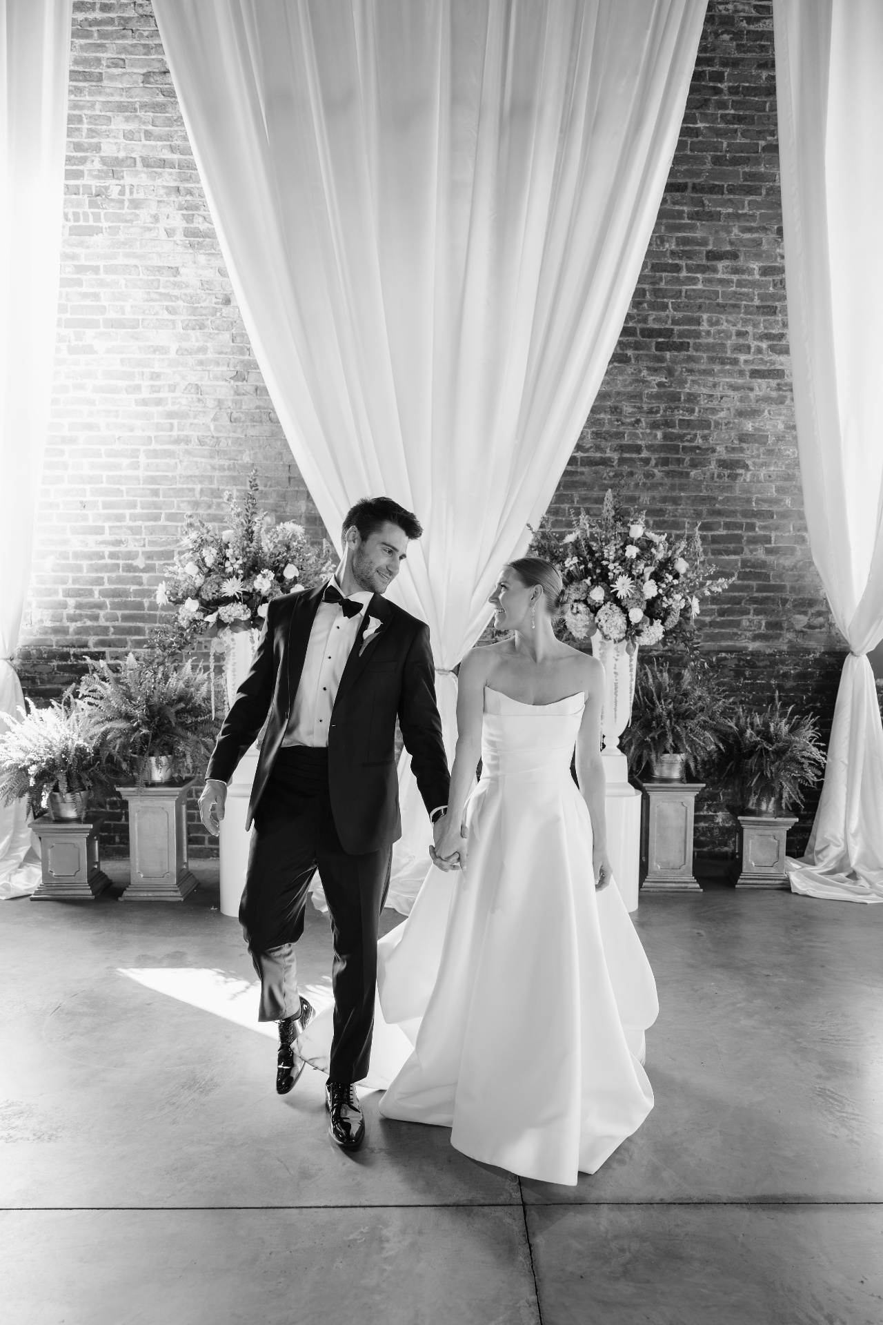 Bride and groom walking hand in hand through ivory drapes
