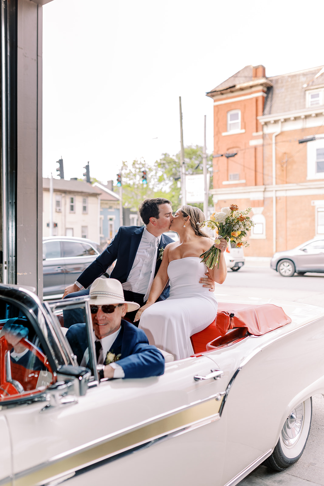 Newlyweds kissing in a vintage convertible outside the venue