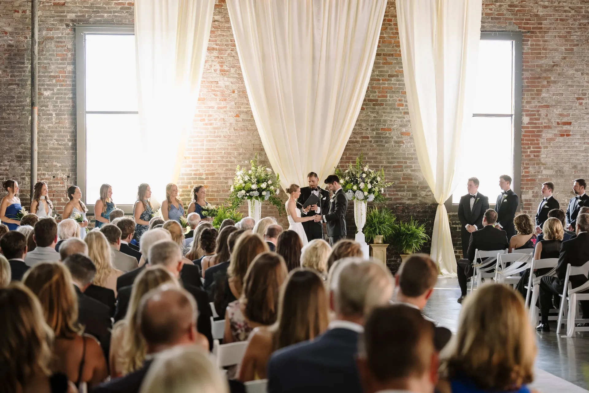 Wedding ceremony with tall ivory drapes against exposed brick