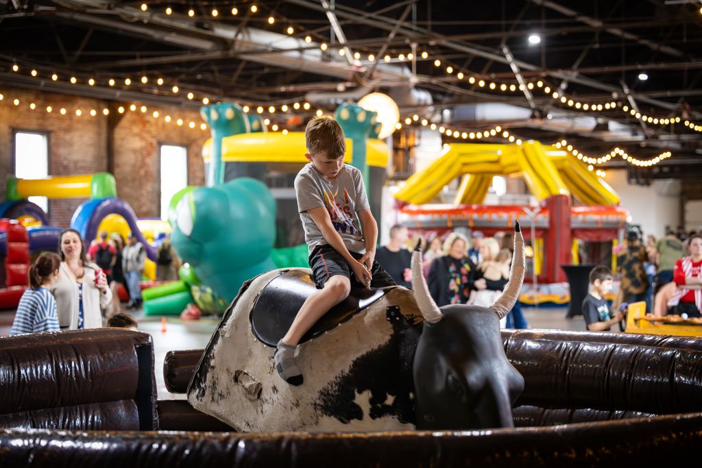 Child riding a mechanical bull at a family event under string lights